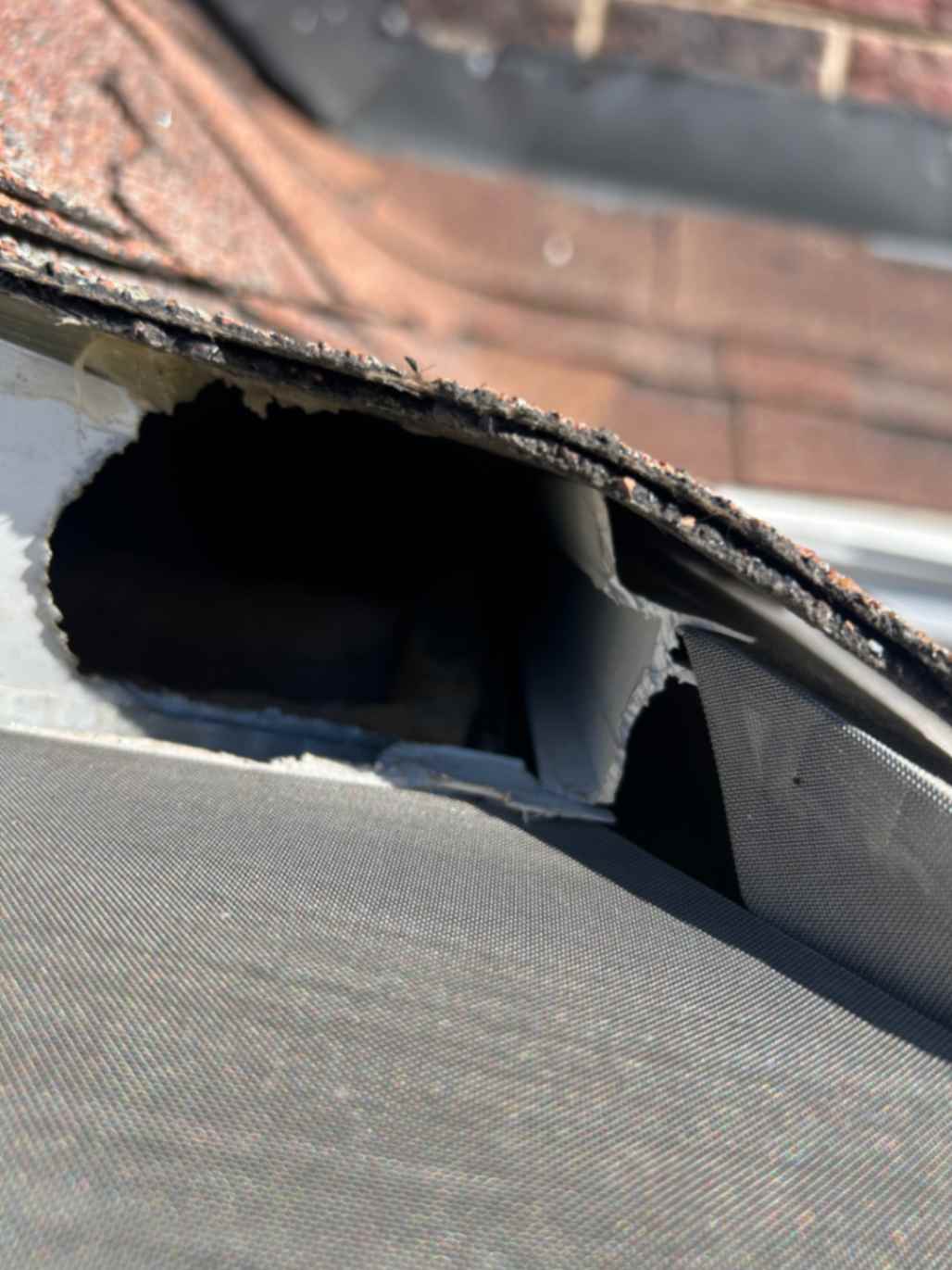 Close-up of damaged roof flashing with a large hole, exposing underlying structure, taken during Squirrel Removal in Clemmons.