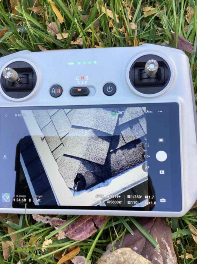 A drone controller on grass displays a screen showing damaged roof shingles, taken during Squirrel Removal in Greensboro.