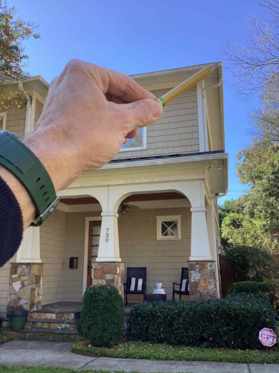 A hand points with a pencil towards the edge of a beige two-story house, taken during Squirrel Removal in Greensboro.