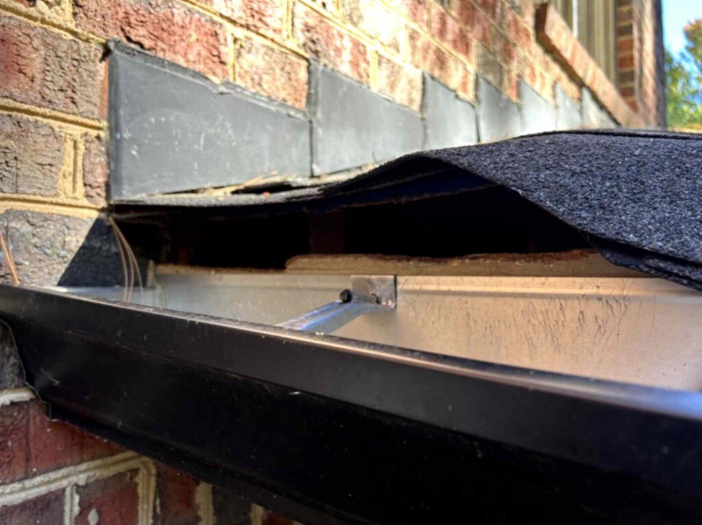 The image shows lifted shingles exposing a gap between the roof and wall, with visible damage near the gutter, taken during Squirrel Removal in Iron Station.