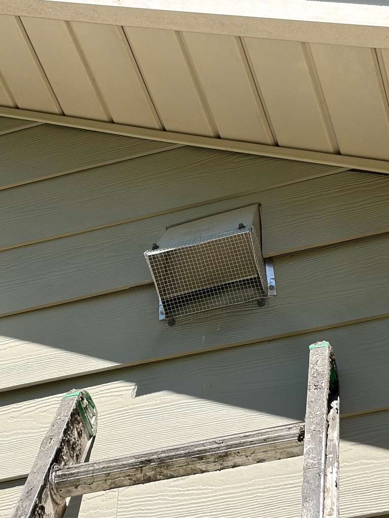 A freshly installed protective wire mesh guard covering an exterior wall vent just above a ladder, a preventative step following bird nest removal from vents Charlotte NC.